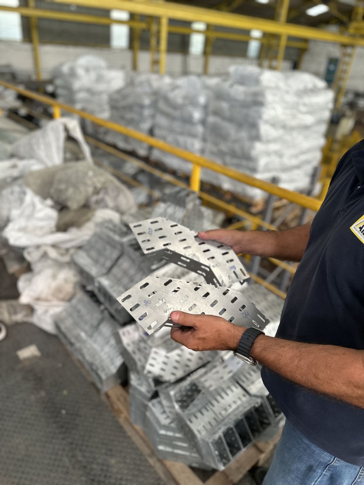 Mão apontando para peças de eletrocalha perfurada recém fabricadas