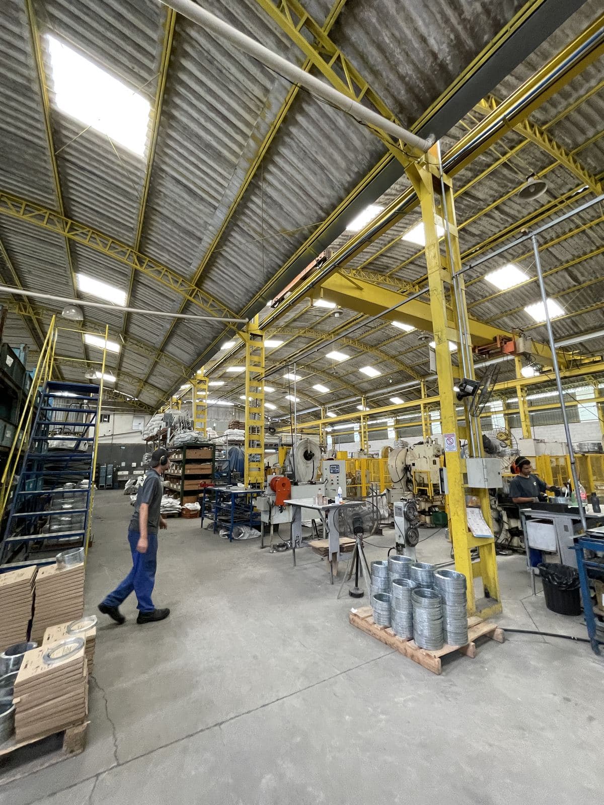 Galpão da fábrica com a estrutura amarela e funcionários trabalhando