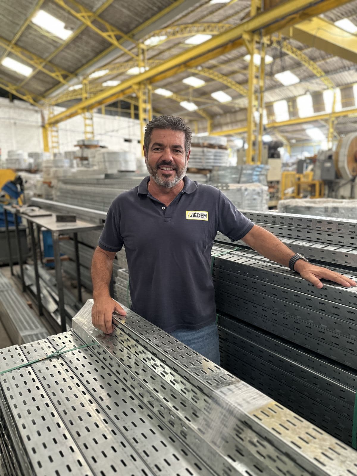 Integrante da Aiédem sorrindo ao lado de eletrocalhas na fábrica